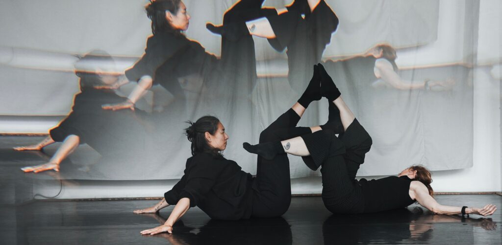 Photo of two dancers touching feet with a projection of their dance behind them.