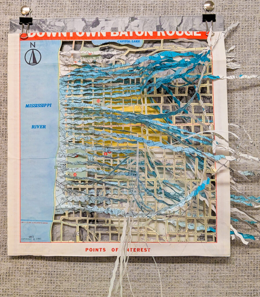 This map, by artist Thien-Kim Bui, explores the intersection of human infrastructureand water. The roads are a skeleton over which the water flows; there is water above and water below. Beneath the water lay memories of landscapes past and dreams of landscapes yet to come. Compass roses from nautical maps respond to unknown magnetisms and contradict each other. Are we looking at a disaster, or an opportunity? The map refuses to answer.